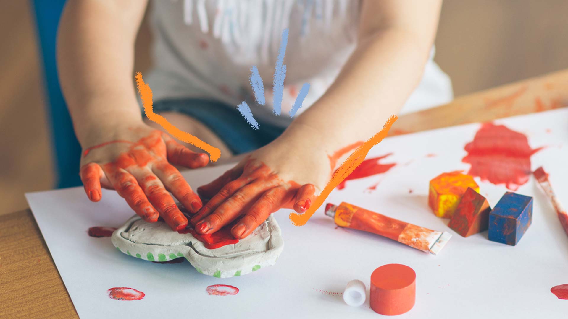 Como fazer tinta caseira: foto de uma criança que está com as mãos sujas de tinta e pinta em cima de uma mesa.