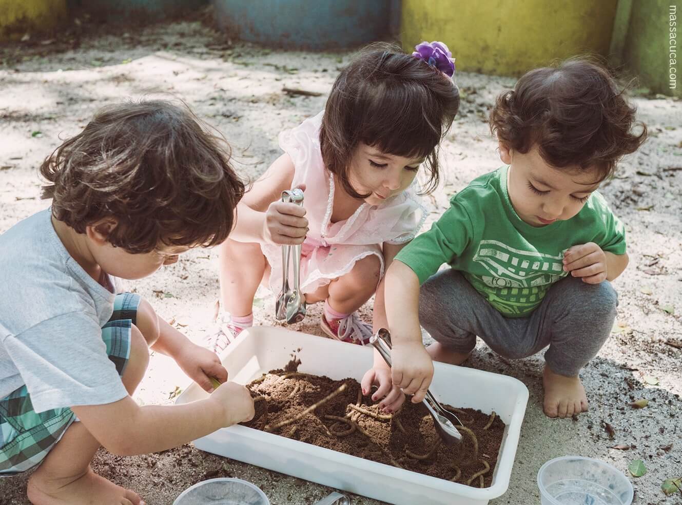 Como fazer um minhocário: foto de três crianças pequenas com cerca de dois anos brincam de mexer na terra.