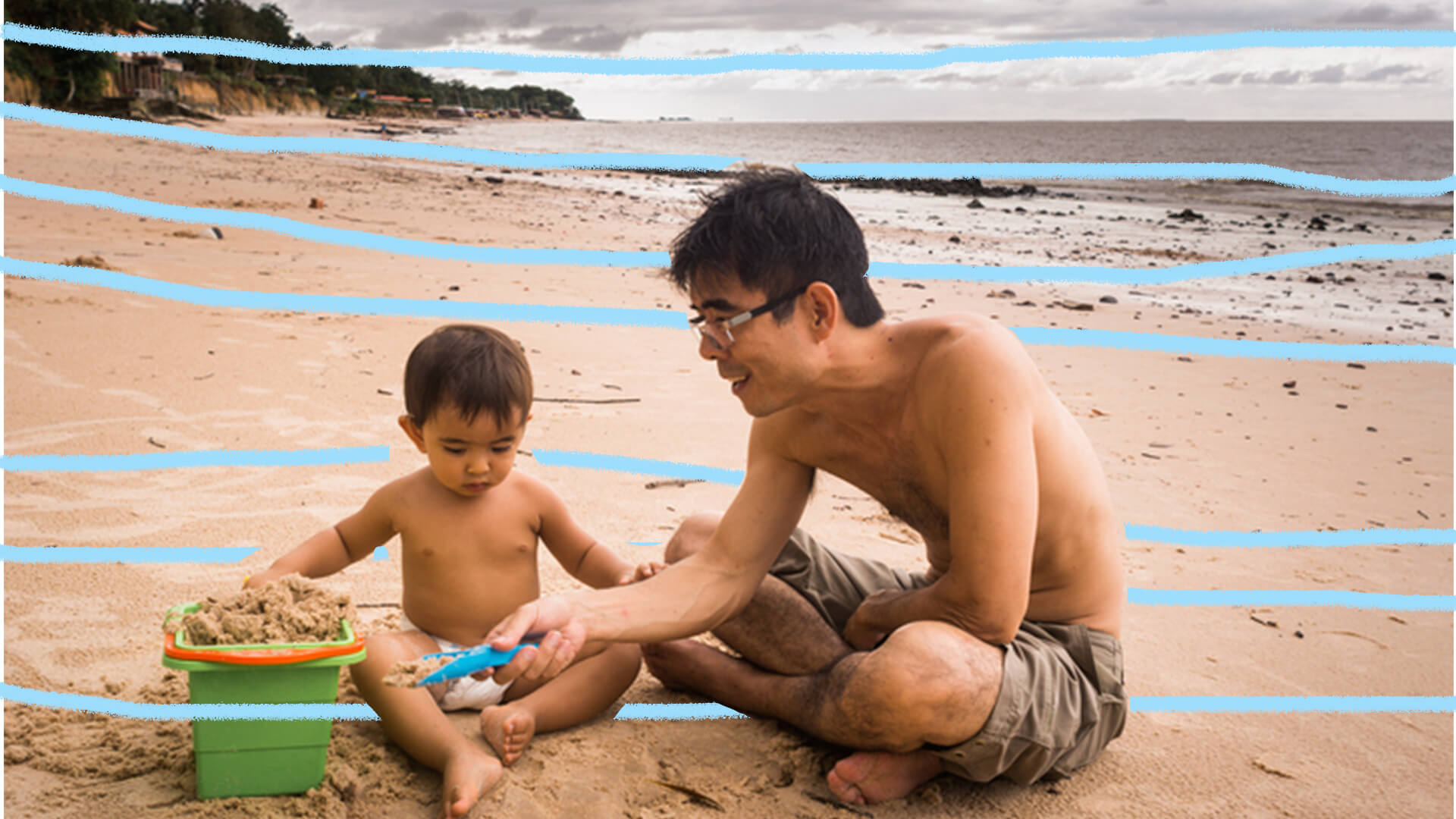 Menino e homem sentados na areia da praia. Vê-se o mar ao fundo.