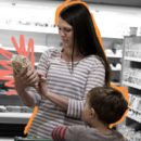 Em um supermercado, uma mulher lê o rótulo de um produto enquanto uma criança a observa.