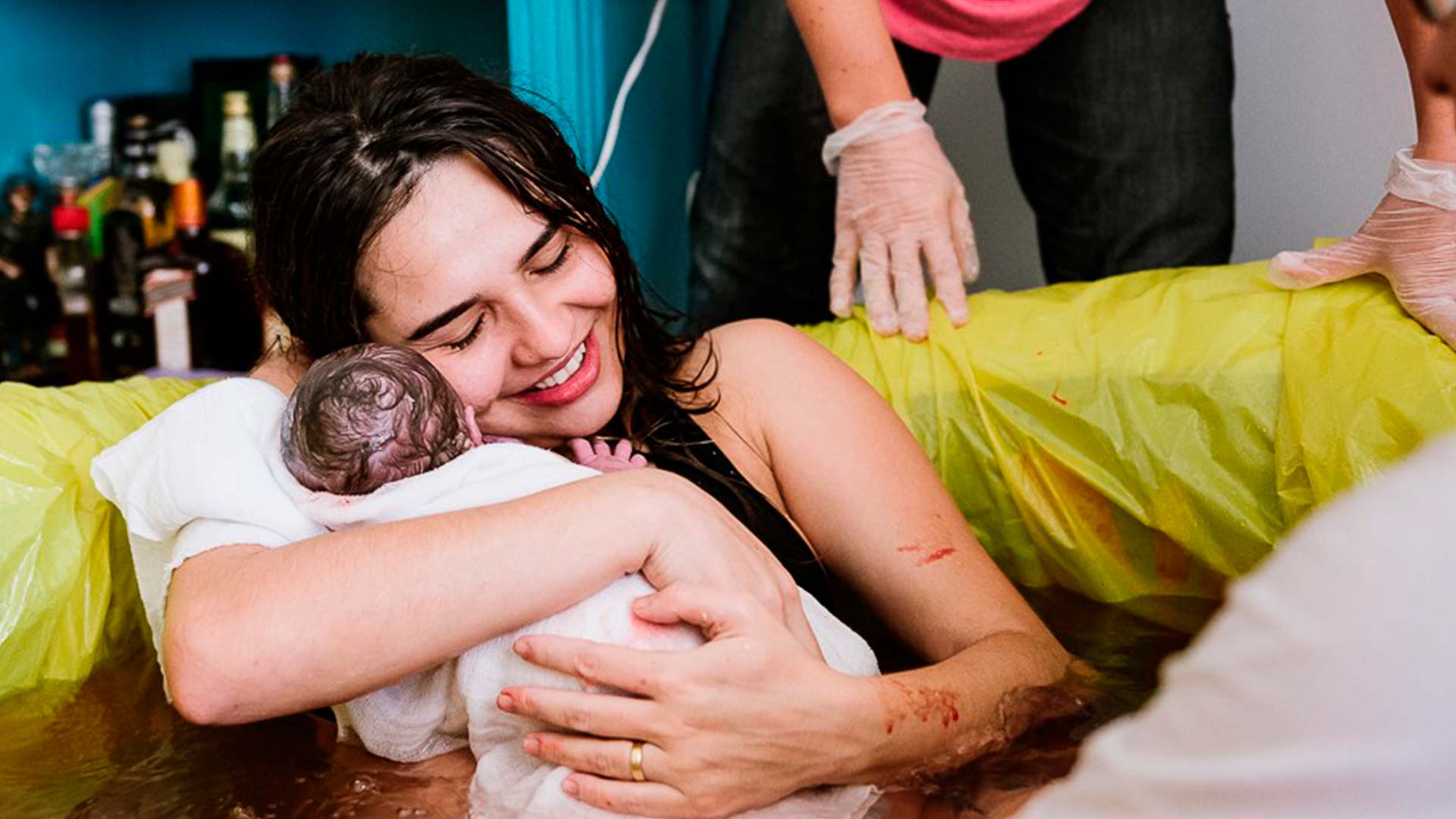 Fotografia de parto: Mãe com filho recém-nascido nos braços, em uma banheira com água.