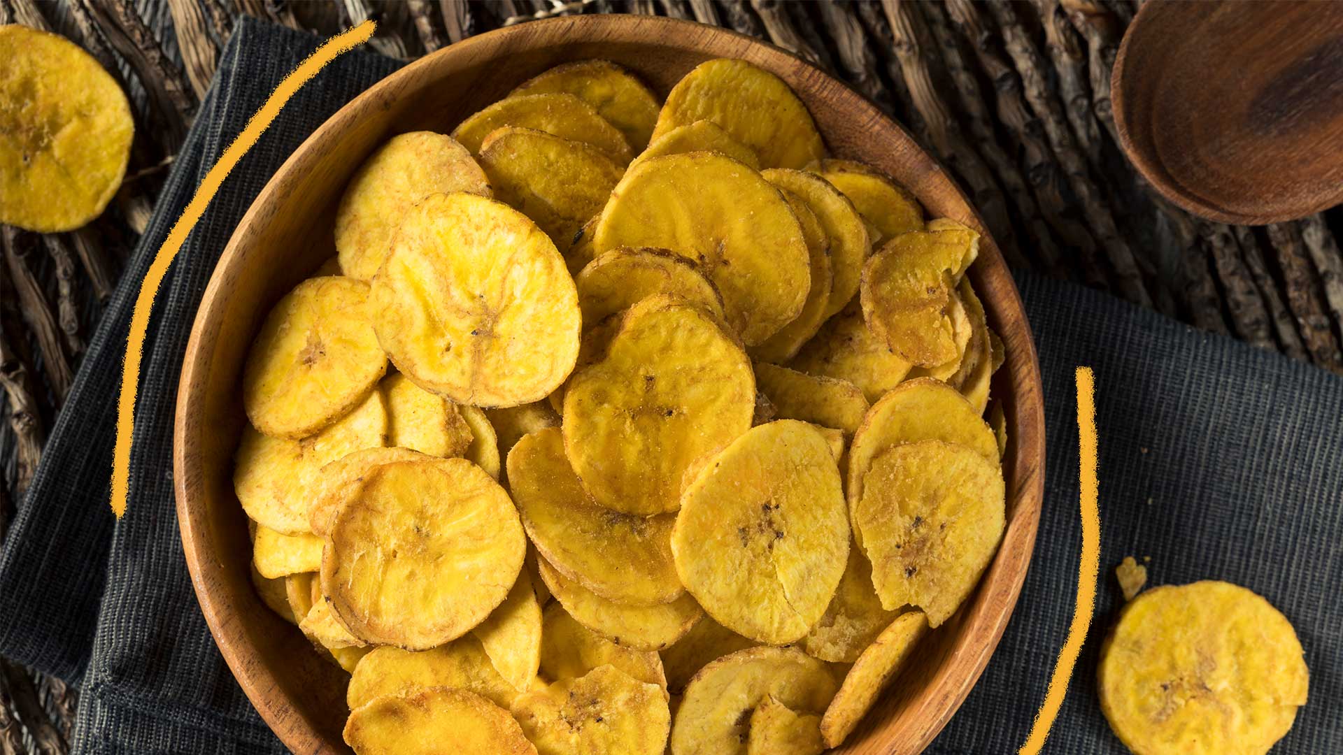 Como fazer chips de banana: foto de um pote de madeira com chips de banana, em cima de uma mesa rústica.