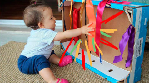 Brincadeiras com caixa de papelão: foto de uma criança que brinca com elementos coloridos colados no papelão.