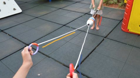 Brinquedo de garrafa pet: foto de duas crianças que brincam com um vai-e-vem, composto por dois barbantes e uma garrafa de leite.