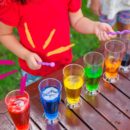 criança tocando xilofone feito de copos de água com diferentes líquidos coloridos.
