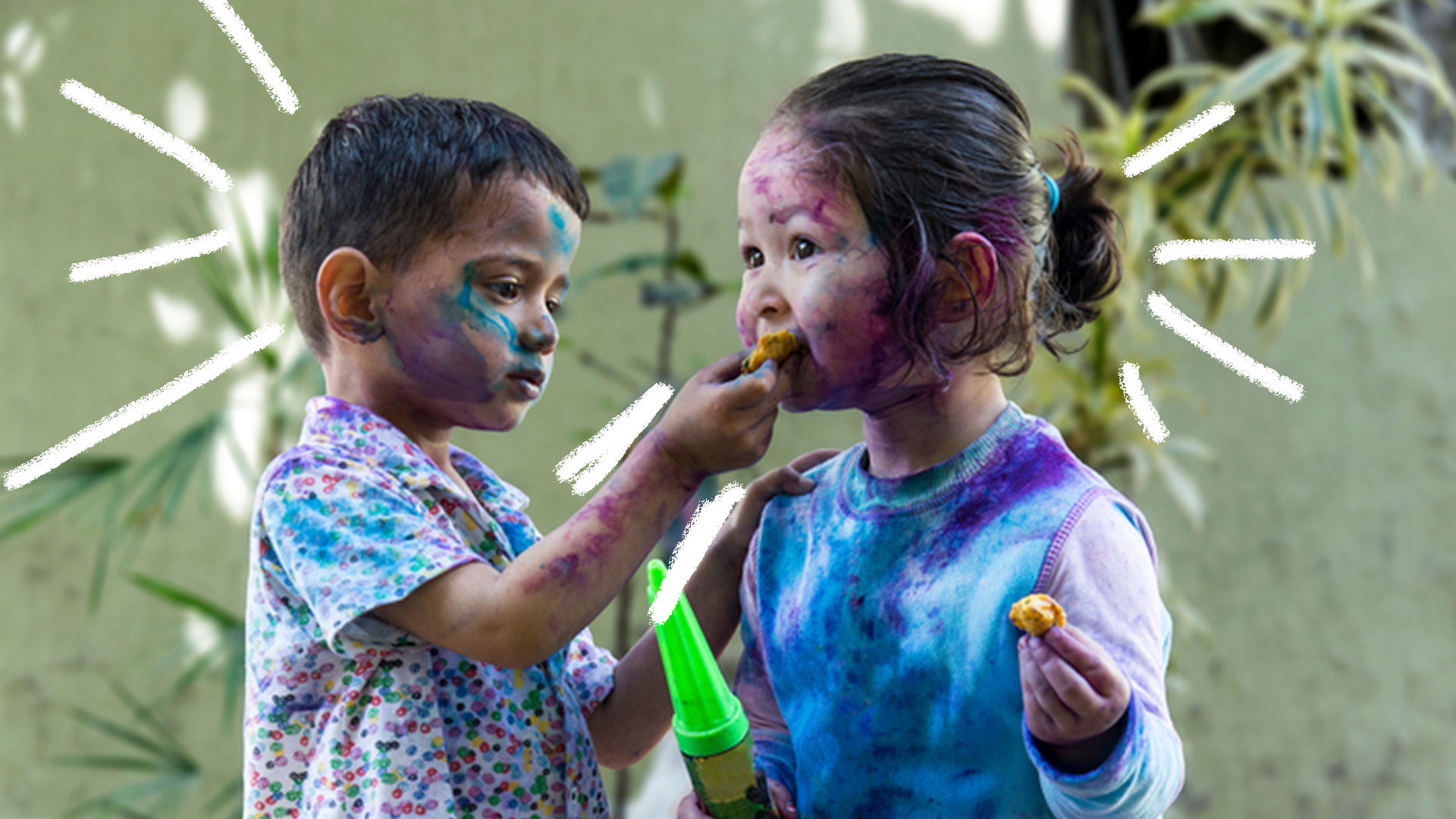 Um menino e uma menina brincando de atirar tinta um no outro no quintal. Eles estão lambuzados de tinta azul e roxa.