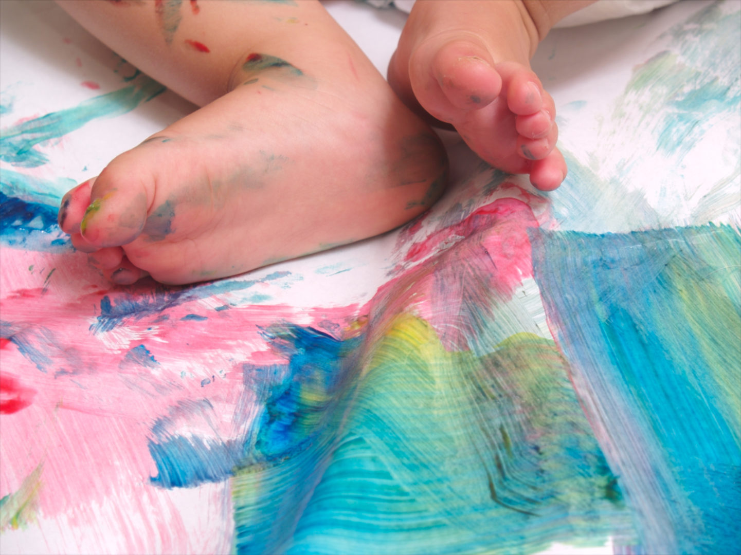 Tintas comestíveis para bebês: foto de pés de um bebê de pele clara em uma superfície com tinta colorida.