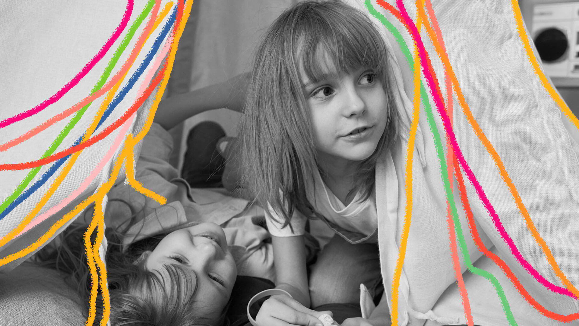 Brincadeiras para amigos em casa: foto de duas meninas que brincam debaixo de uma cabaninha de pano montada na sala. Grafismos coloridos enfeitam a imagem.