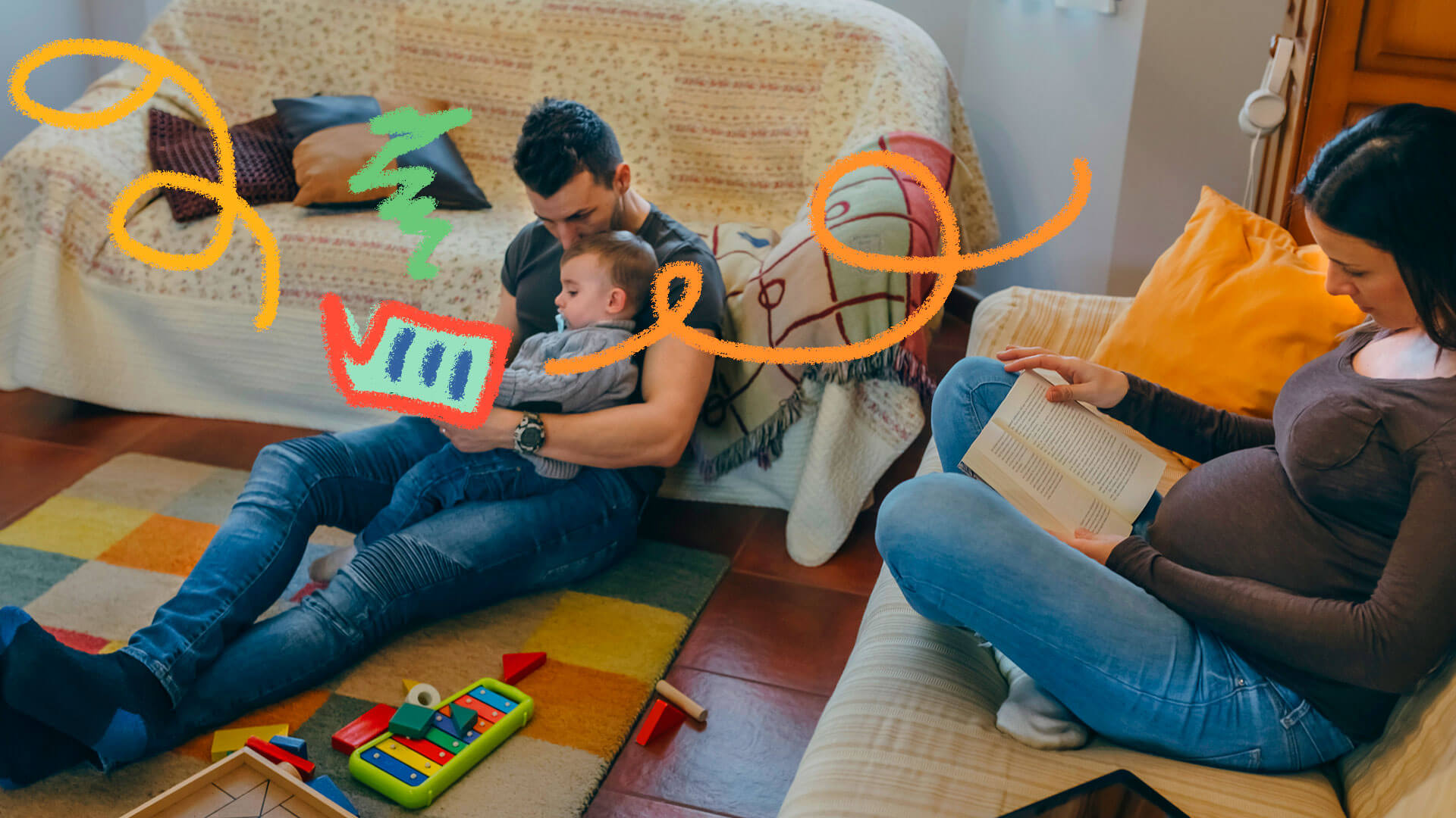 Sentados numa sala com brinquedos espalhados pelo chão, um pai e um bebês leem um livro. No sofá ao lado, a mãe também lê um livro.