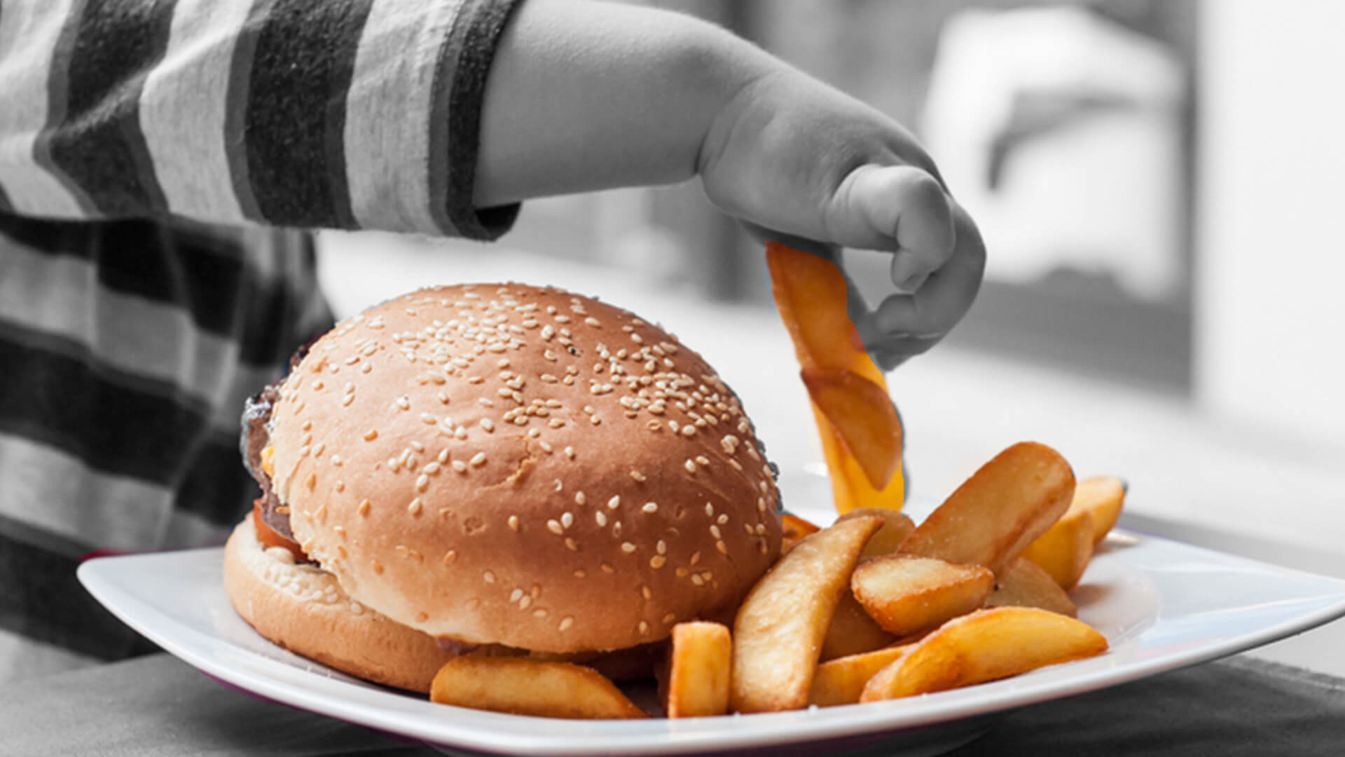 Mão de um bebê pegando uma batata frita ao lado de um hambúrguer