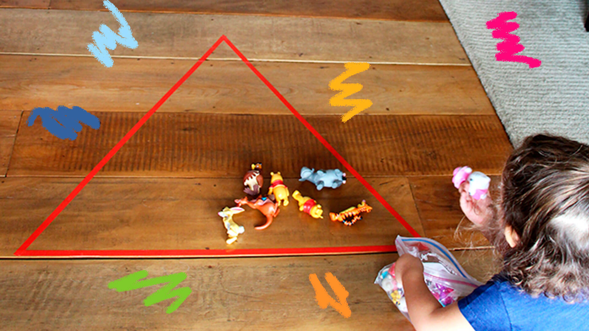 Uma criança brinca no chão com fita crepe e miniaturas de brinquedos