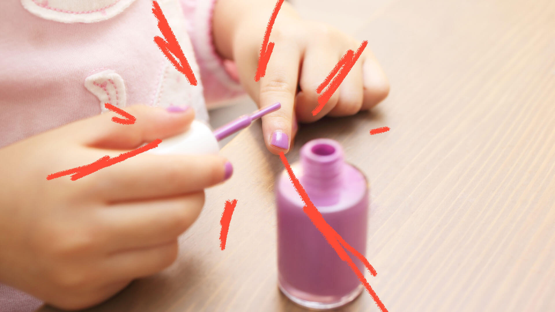 Em primeiro plano, a mão de uma criança passando esmalte