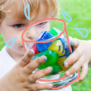Foto mostra um menino segurando com as duas mãos um recipiente redondo com gelos sensoriais.