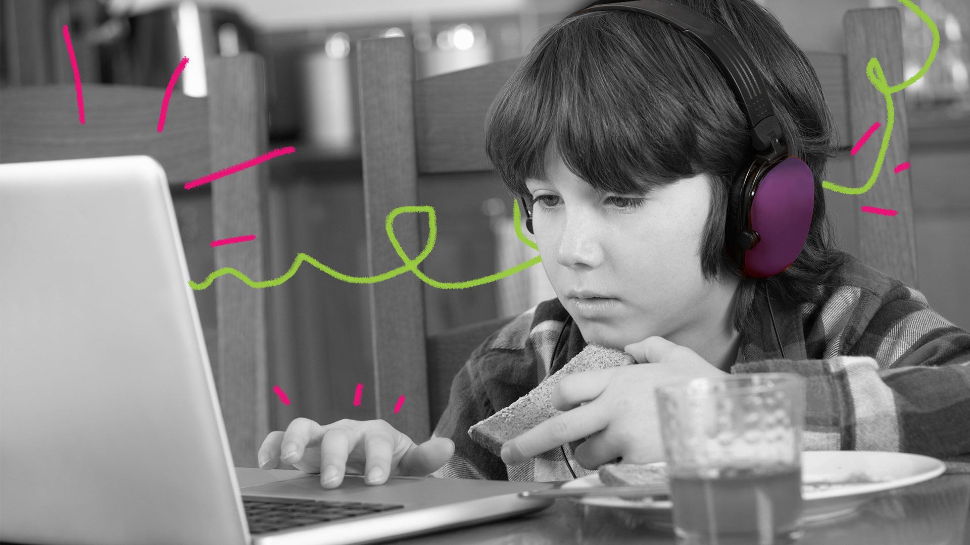 Menino em frente ao notebook olha concentrado a tela e utiliza um headfone roxo nos ouvidos.