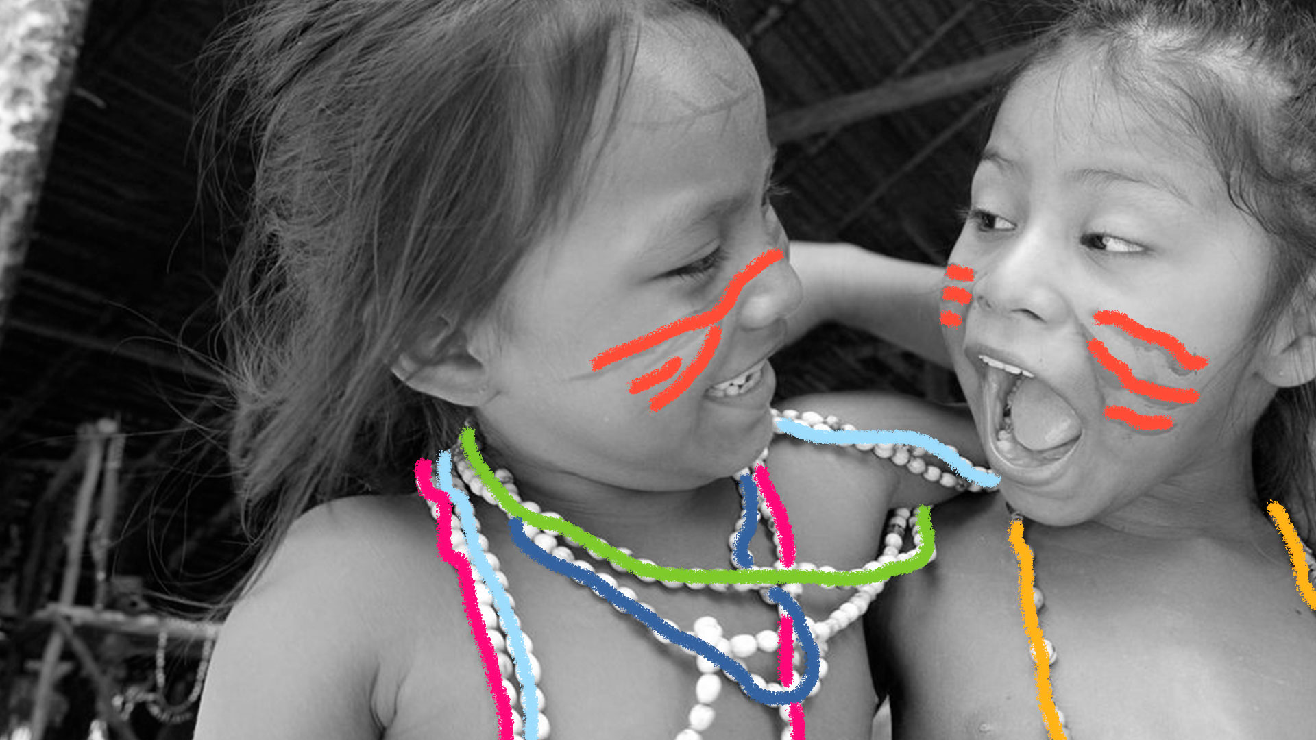 Foto em preto e branco mostra duas meninas índias. A da esquerda sorri enquanto a da direita se prepara, com a boca aberta, para falar alguma coisa.