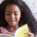 Menina negra lendo um livro sorrindo.