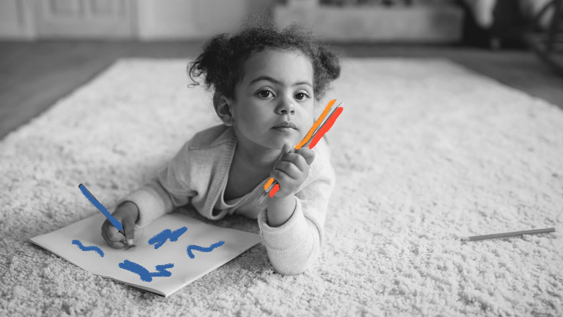 Deitada em um tapete no chão da sala, uma menina negra está desenhando com lápis de cor de diferentes cores.