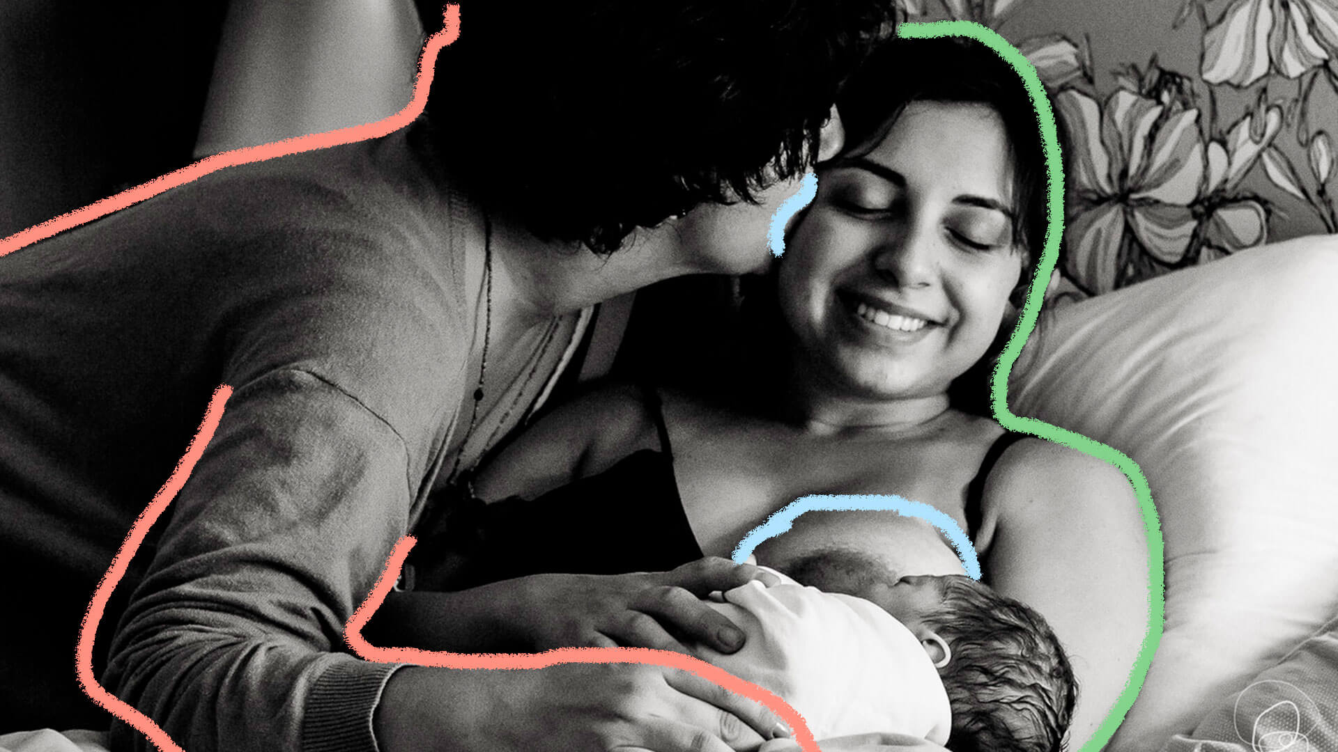 Um homem beija a cabeça de uma mulher, que está amamentando seu bebê. A imagem está em preto e branco.