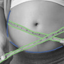 Barriga de uma mulher grávida com uma fita métrica medindo o tamanho da barriga.