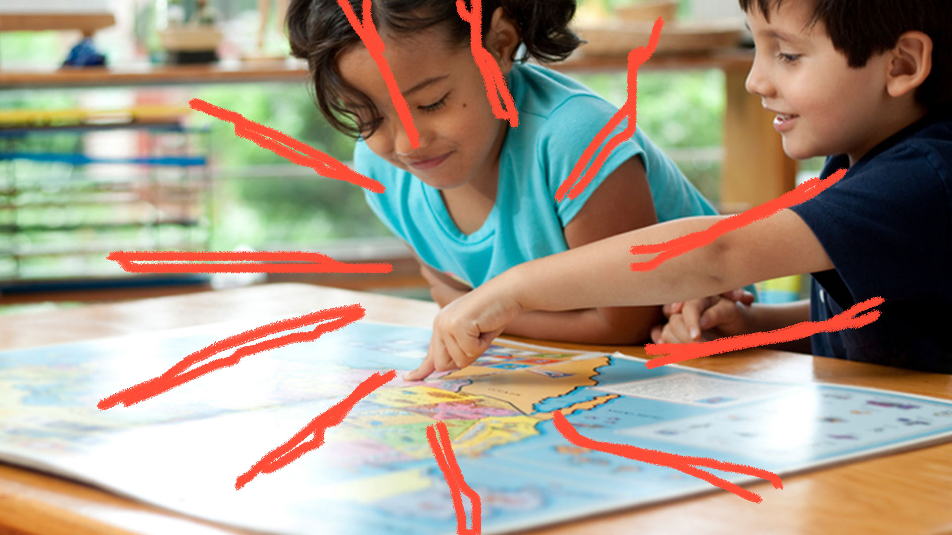 Duas crianças observam e apontam para um mapa aberto em cima de uma mesa. A esquerda está uma menina de camiseta azul clara e a direita um menino de camiseta azul escura.