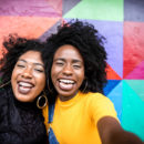 Duas mulheres negras tirando selfie em um uma parede colorida
