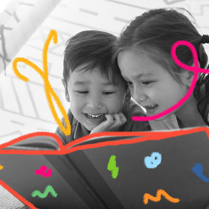 Um menino e uma menina estão brincando de cabaninha e lendo um livro. Os dois estão sorrindo e parecem deslumbrados.