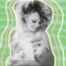 Foto em preto e branco. Mulher de cabelo cacheado amamenta um bebe que está segurando no colo.