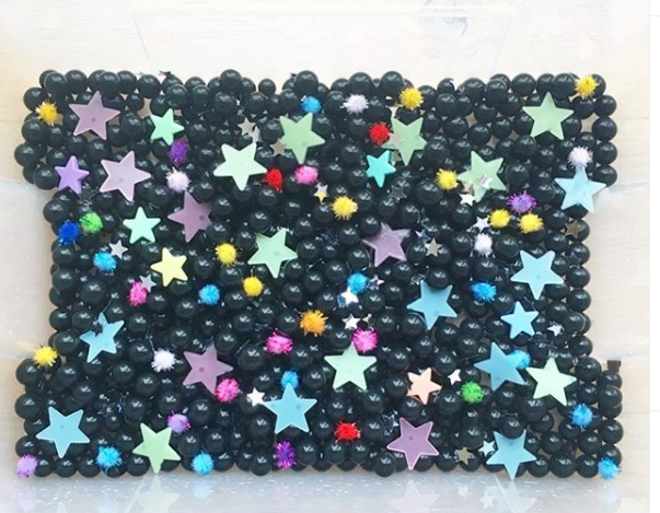 Astronomia divertida: Uma caixa com várias bolinhas pretas e estrelas de papel espalhadas