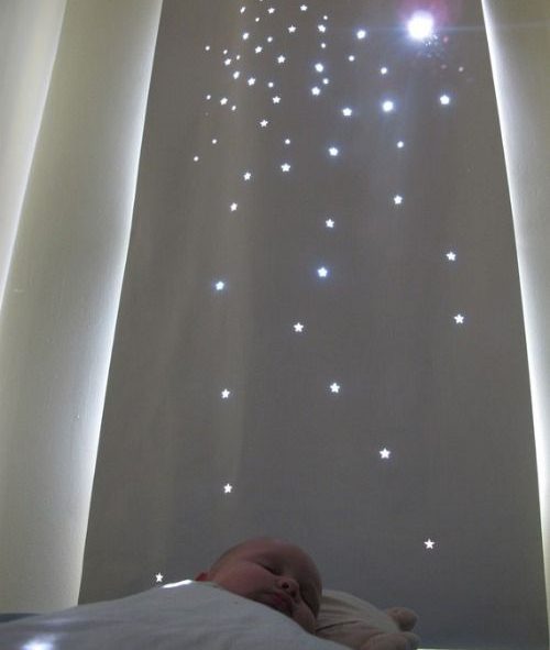 Cortina com vários furos em formato de estrela e um bebê dorme na cama, à frente da cortina