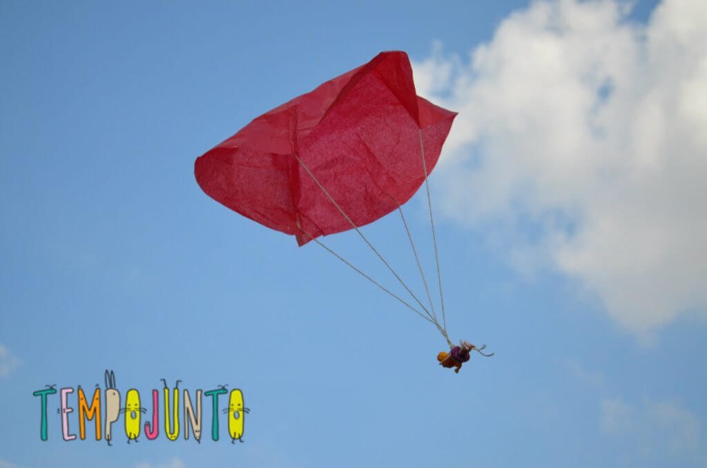 Em um céu azul, um pequeno paraquedas de brinquedo feito de papel vermelho