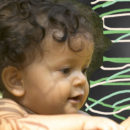 Perfil de um bebê, com cabelos enrolados e castanhos.