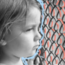 Evitar o bullying: Foto do rosto de uma criança em preto e branco com um olhar triste. Ela está olhando fixamente através de uma rede de proteção