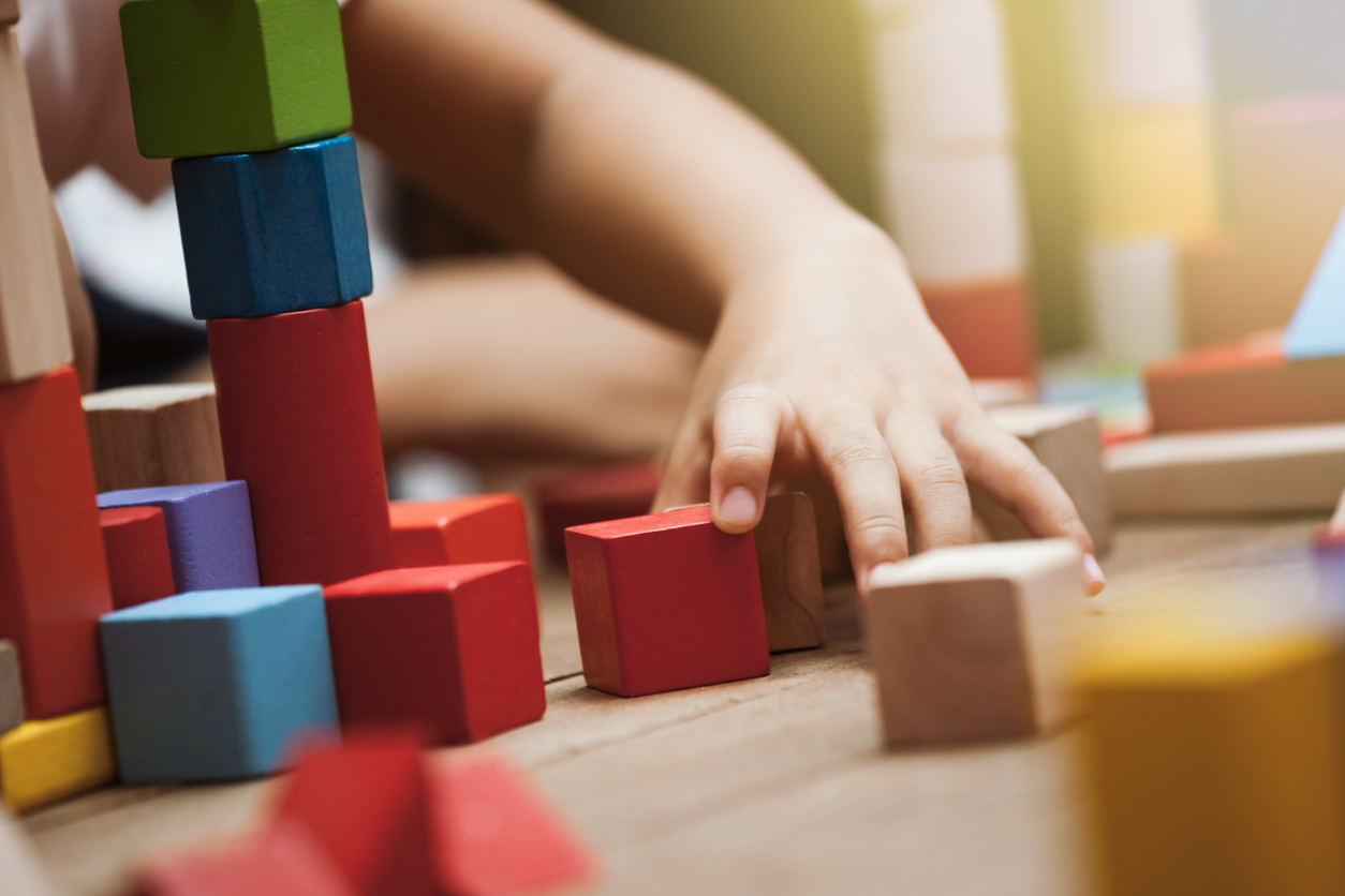 Mãos de criança brincando com blocos de montar de madeira colorida.