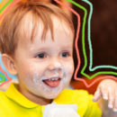 Danoninho de inhame: Menino com cerca de 3 anos segurando um pote de iogurte. Seu rosto está lambuzado do creme e ele está sorrindo.