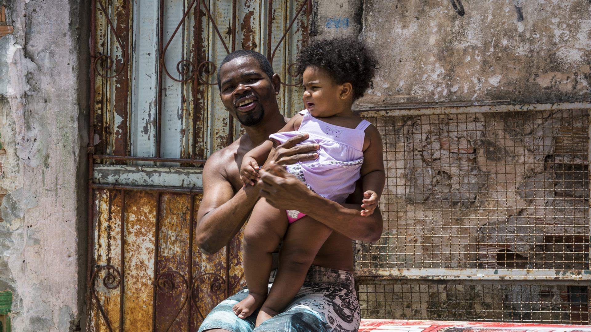 Pai com filha bebê no colo em favela