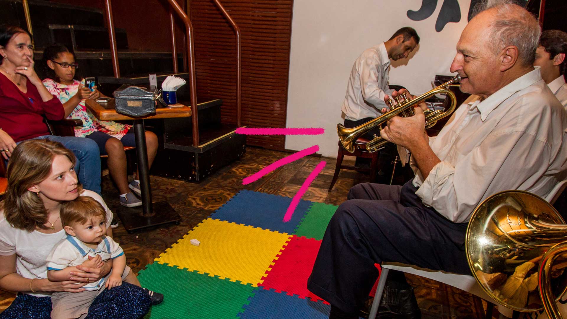 Sair com crianças></noscript> foto de um lugar em que um homem toca um instrumento musical e, no chão, há um piso colorido.