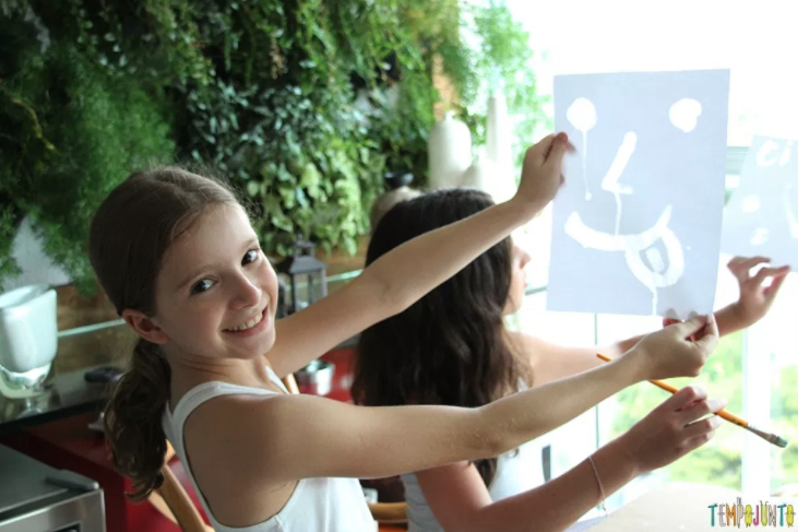 arte para crianças: foto de uma menina sorrindo com uma pintura feita em papel nas mãos