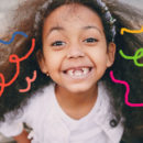Imagem de uma menina de cabelos compridos e encaracolados aparece em primeiro plano sorrindo para a foto. Da sua cabeça, grafismos coloridos simulam fios de cabelo.