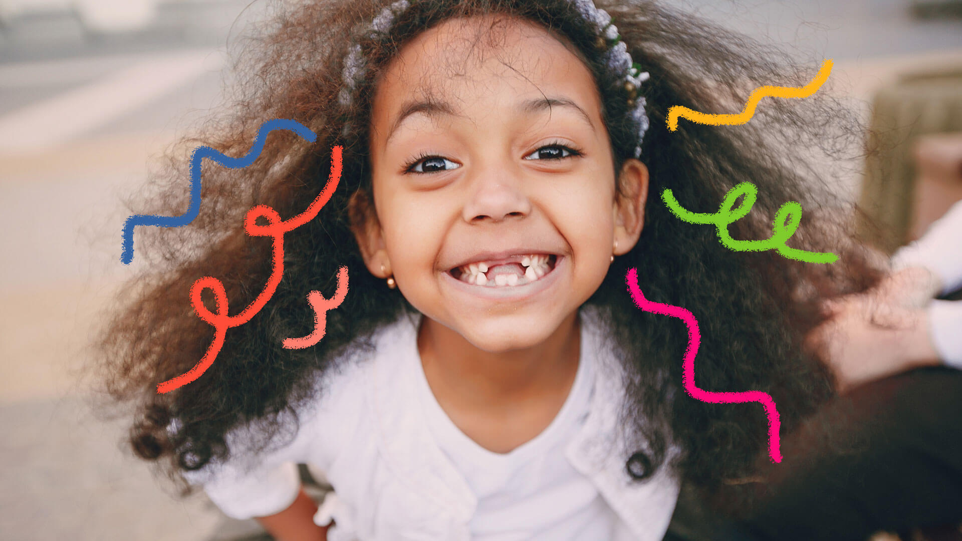 Imagem de uma menina de cabelos compridos e encaracolados aparece em primeiro plano sorrindo para a foto. Da sua cabeça, grafismos coloridos simulam fios de cabelo.