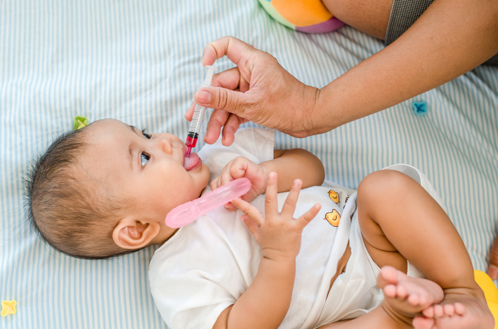 Foto de uma mãe de adulto introduzindo algum líquido dentro de uma seringa na boca de um bebê