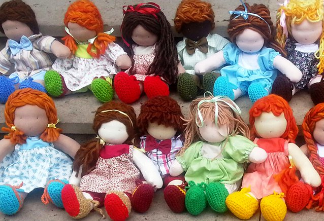 Diferentes e diversas bonecas de pano posicionadas lado a lado. Elas são feitas de tecidos coloridos e têm diferentes cores de cabelo e de pele.