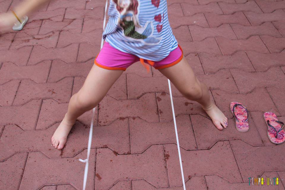 Foto mostra pés de menina na brincadeira de pular elástico
