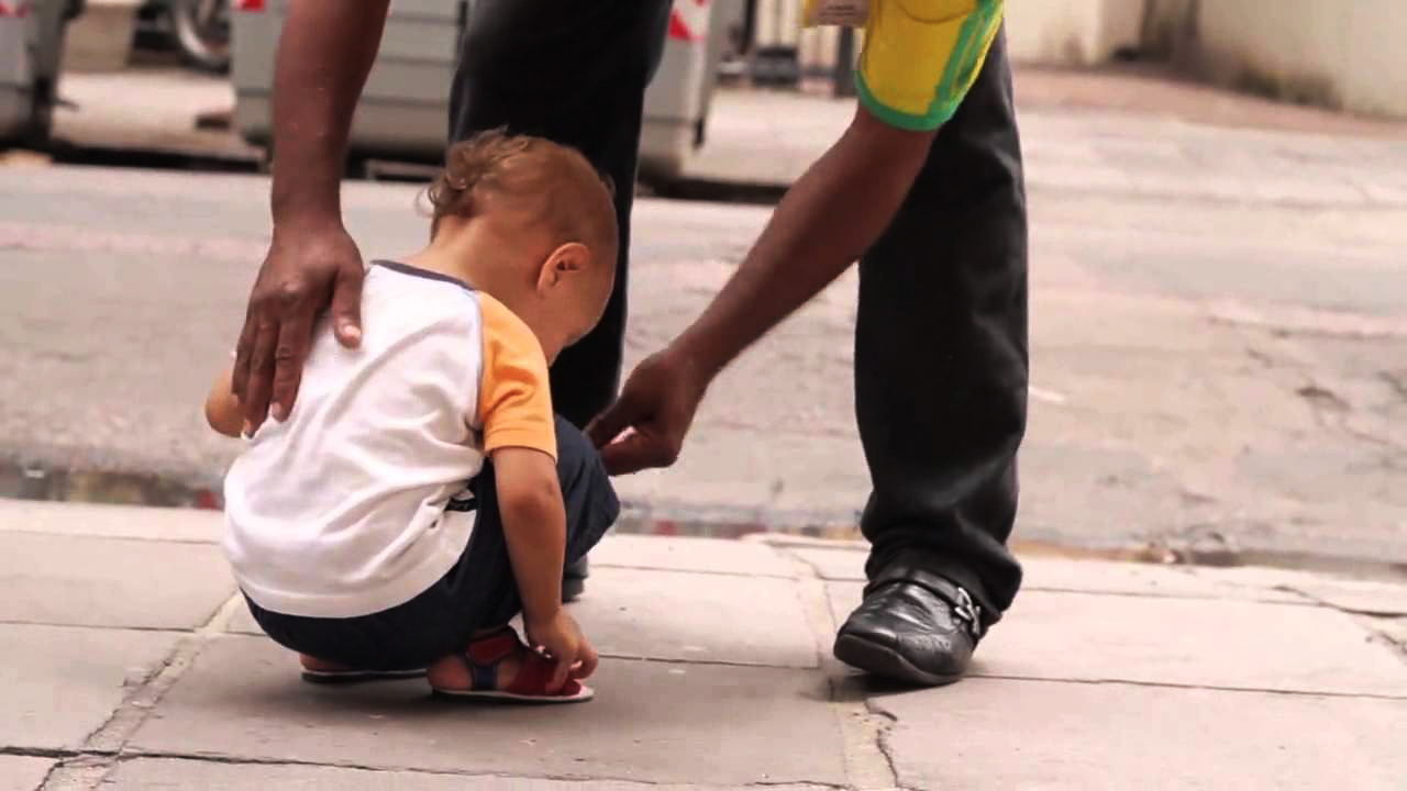 Caminhando com Tim Tim: foto de uma criança agachada, que olha para o chão, e ao lado há um adulto que está com a mão em suas costas.