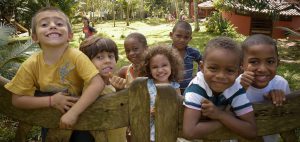 Crianças sorrindo apoiadas em uma cerca de madeira.