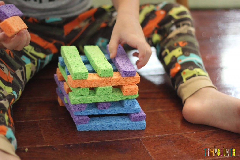 Criança sentada no chão formando uma torre com pedaços de esponjas coloridas