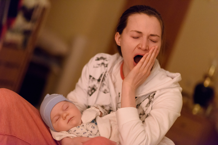 horas de sono: foto de uma mãe bocejando com um bebê no colo