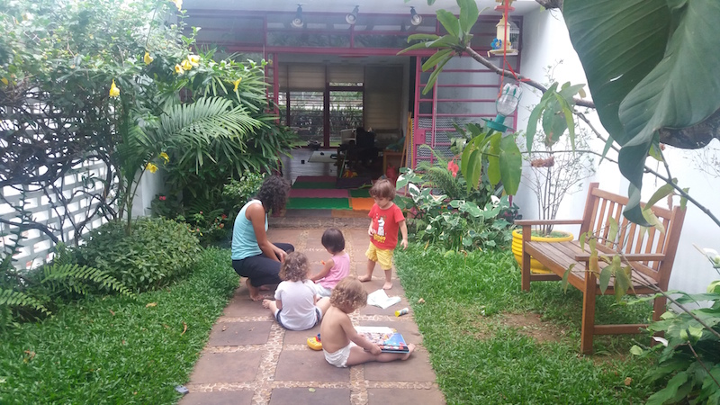 Um quintal com gramado e plantas com crianças brincando.