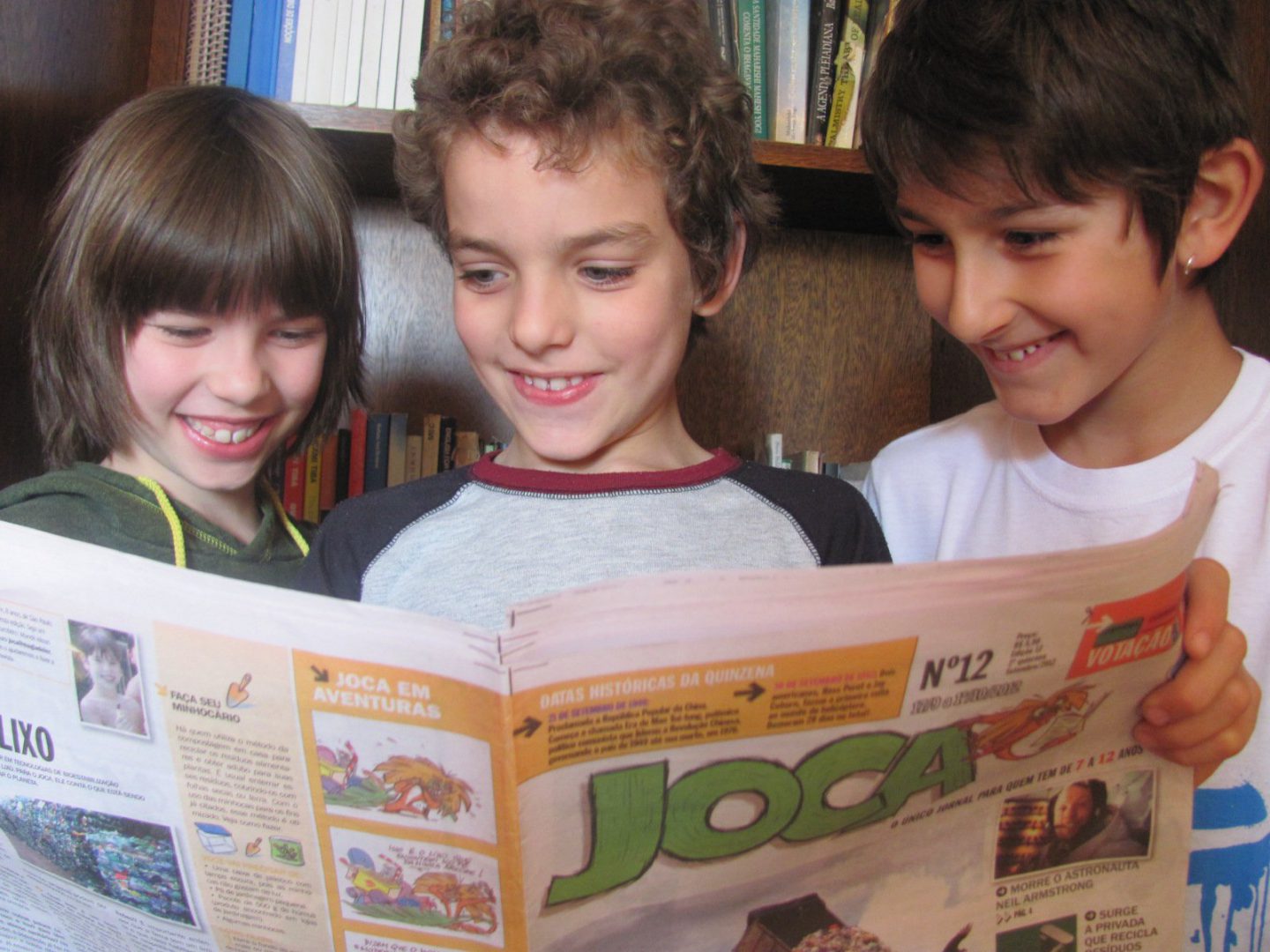Três crianças estão lendo uma edição do Joca e sorrindo