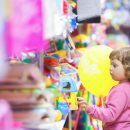 Foto de uma criança em uma loja de brinquedos cheia de brinquedos diversos. Ela olha com uma cara paralisada para os brinquedos