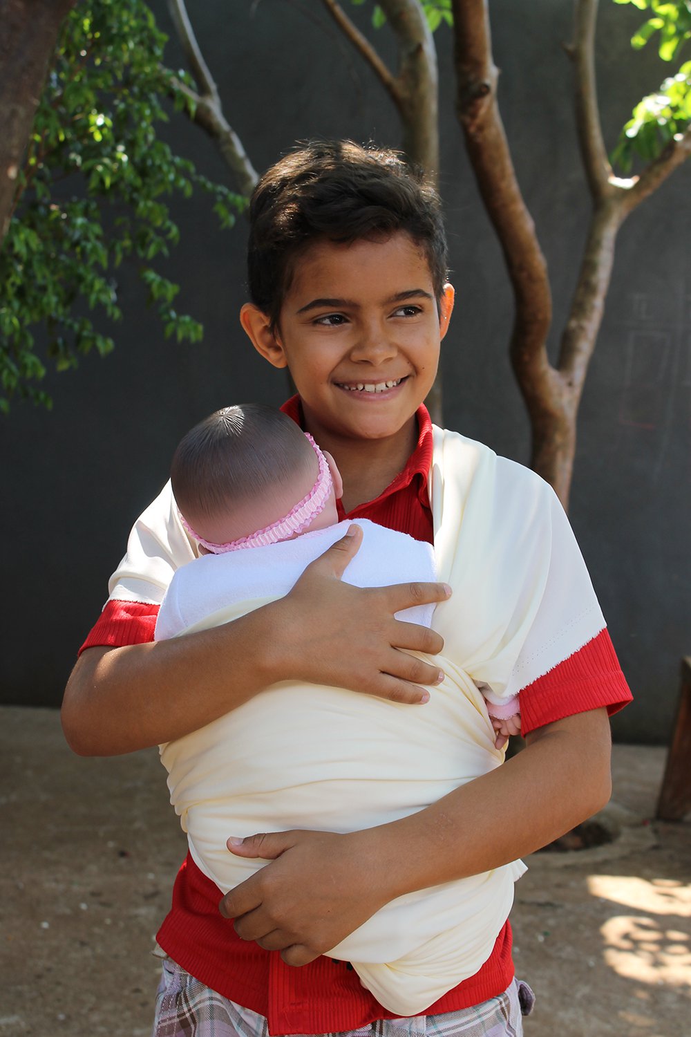 Um garoto com cerca de 10 anos carrega um bebê de faz de conta em um sling